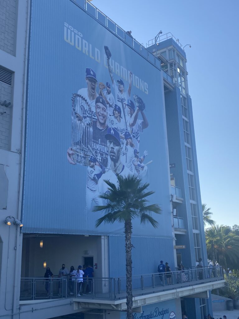 A giant "2020 World Champions" banner showing Dodgers players and the championship trophy hangs on the Dodger Stadium exterior.