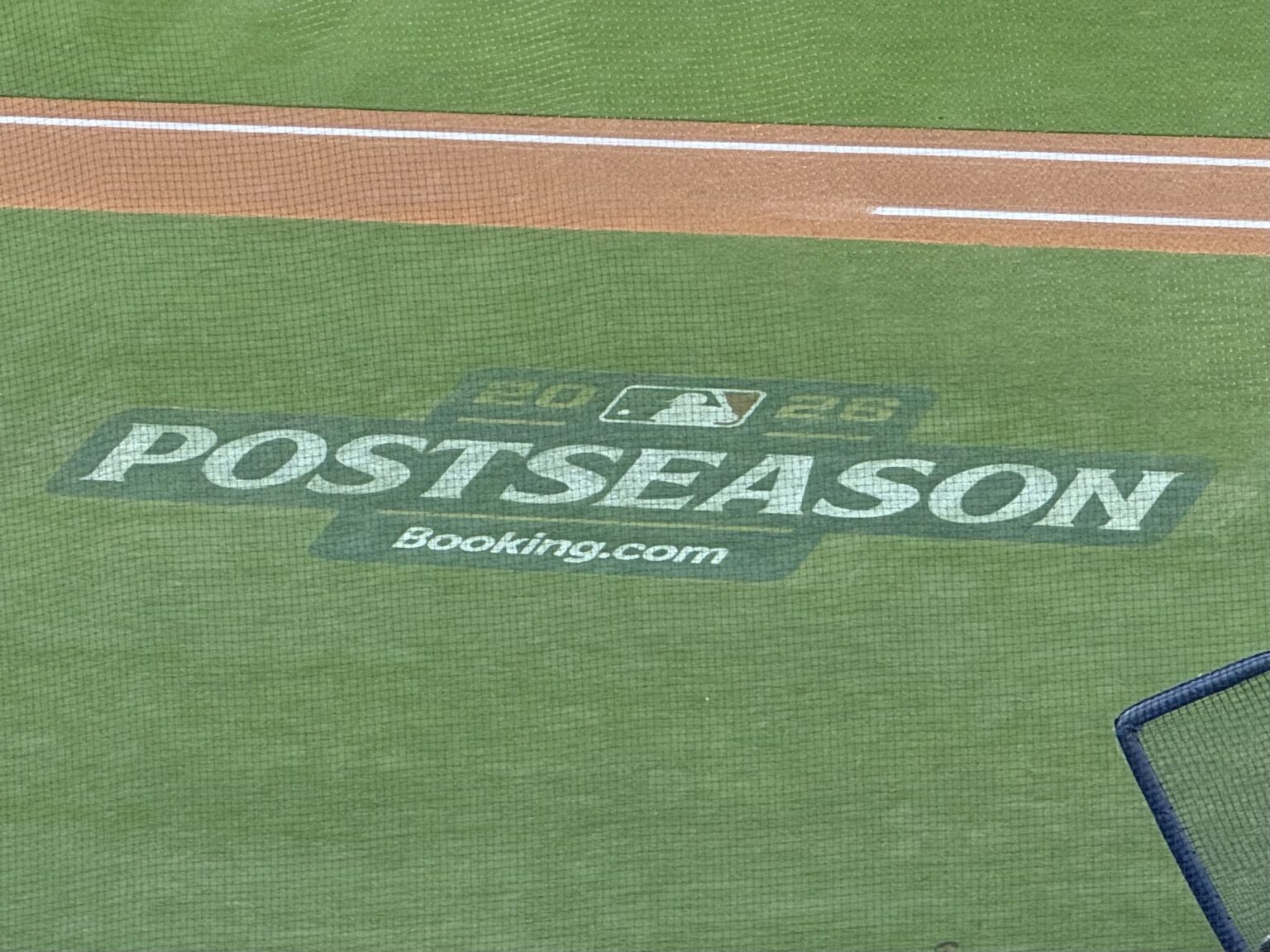 Dodgers take NLDS Game 3, can clinch Wednesday afternoon A "2026 Postseason" logo with Booking.com branding painted on the grass along the baseline at Dodger Stadium, seen through the backstop netting.