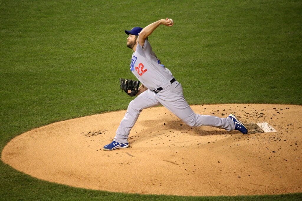 Clayton Kershaw in a gray Dodgers road uniform striding forward as he throws a pitch from the mound.
