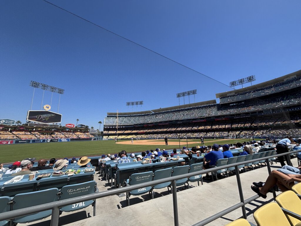 Fans in the Lexus Baseline Club seats watch a sunny day game at Dodger Stadium from behind the protective netting.