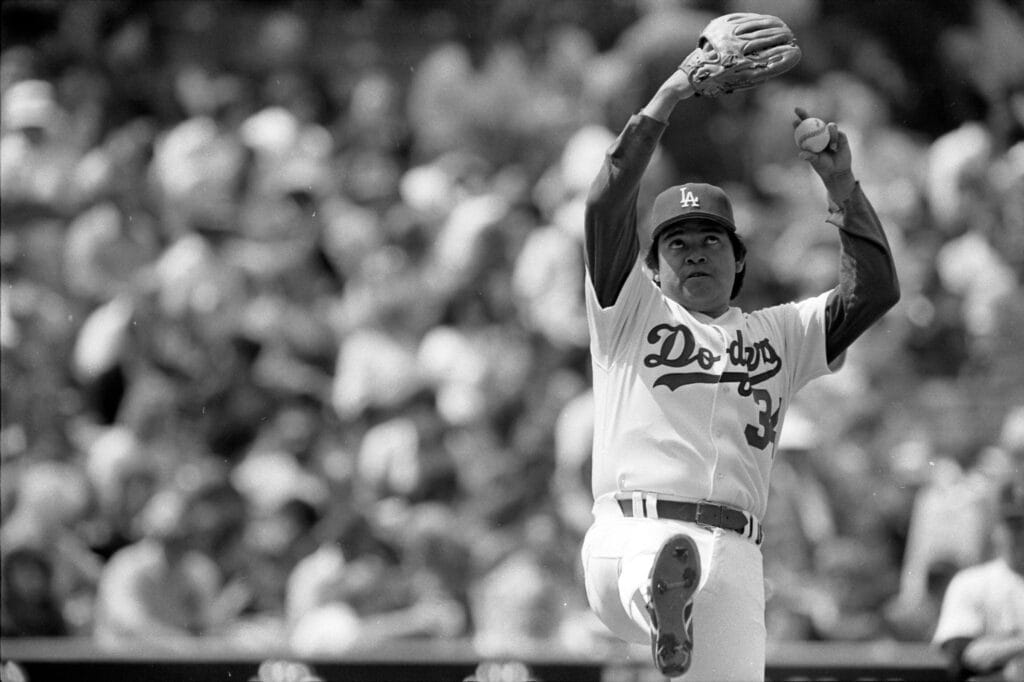 Black-and-white photo of Fernando Valenzuela with his arms raised overhead in his pitching windup.