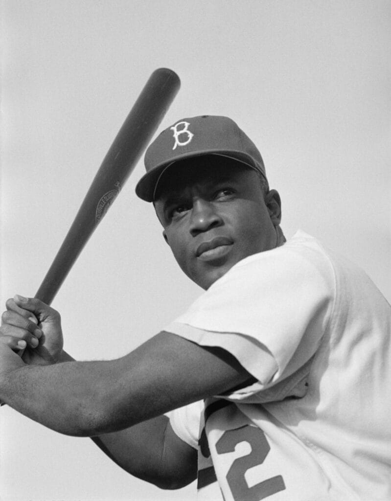 Black-and-white photo of Jackie Robinson in a Brooklyn Dodgers cap holding a bat over his shoulder.