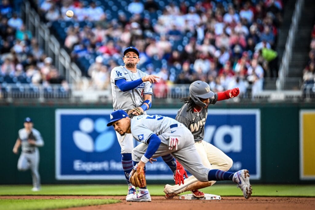 Miguel Rojas stepping on second base and throwing as a sliding Nationals runner comes in, with a Dodgers teammate behind him.