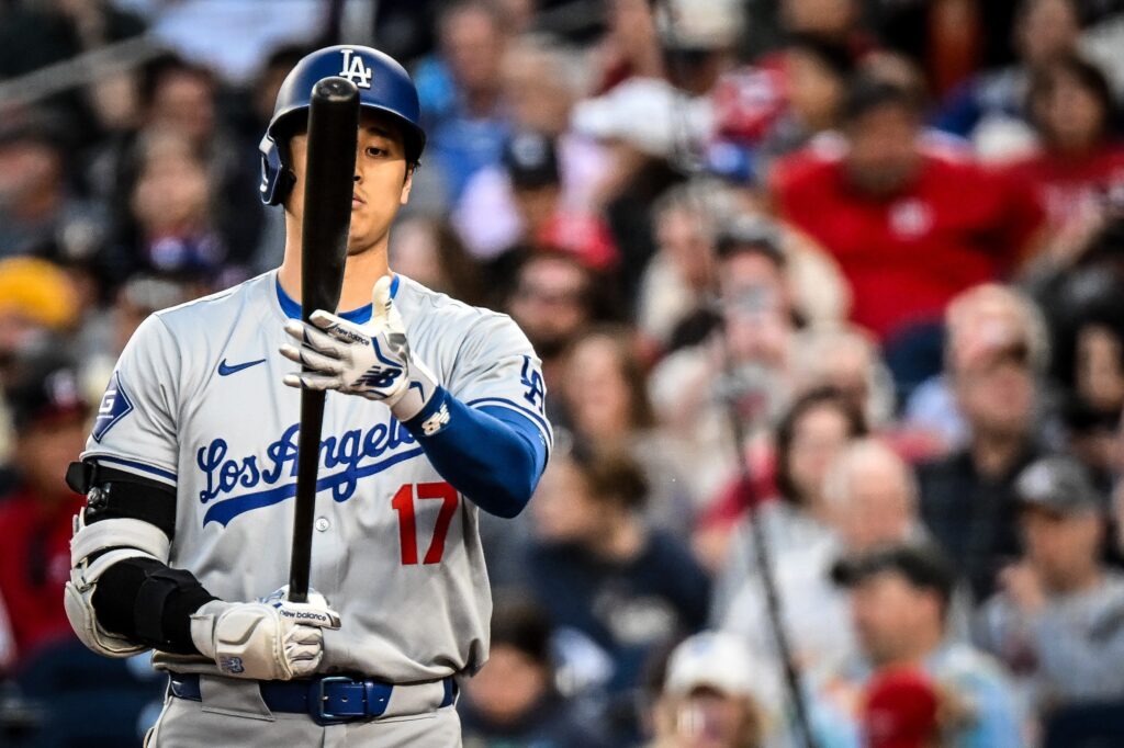 Shohei Ohtani in a gray Los Angeles road jersey with number 17 holding his bat upright and looking at it.