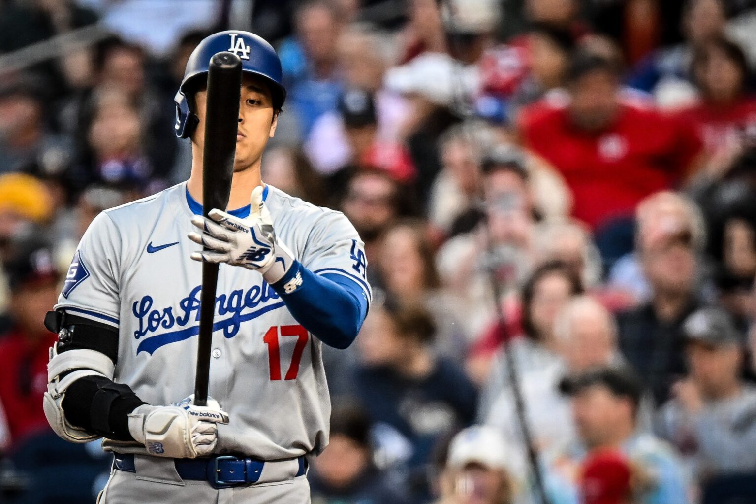 Shohei Ohtani in a gray Los Angeles road jersey with number 17 holding his bat upright and looking at it.