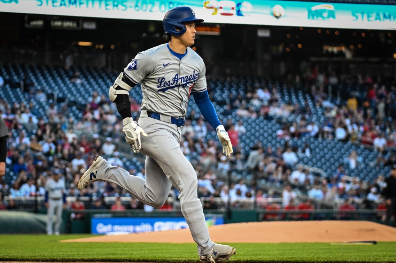 Shohei Ohtani in a gray Dodgers road uniform and blue helmet running on the field.