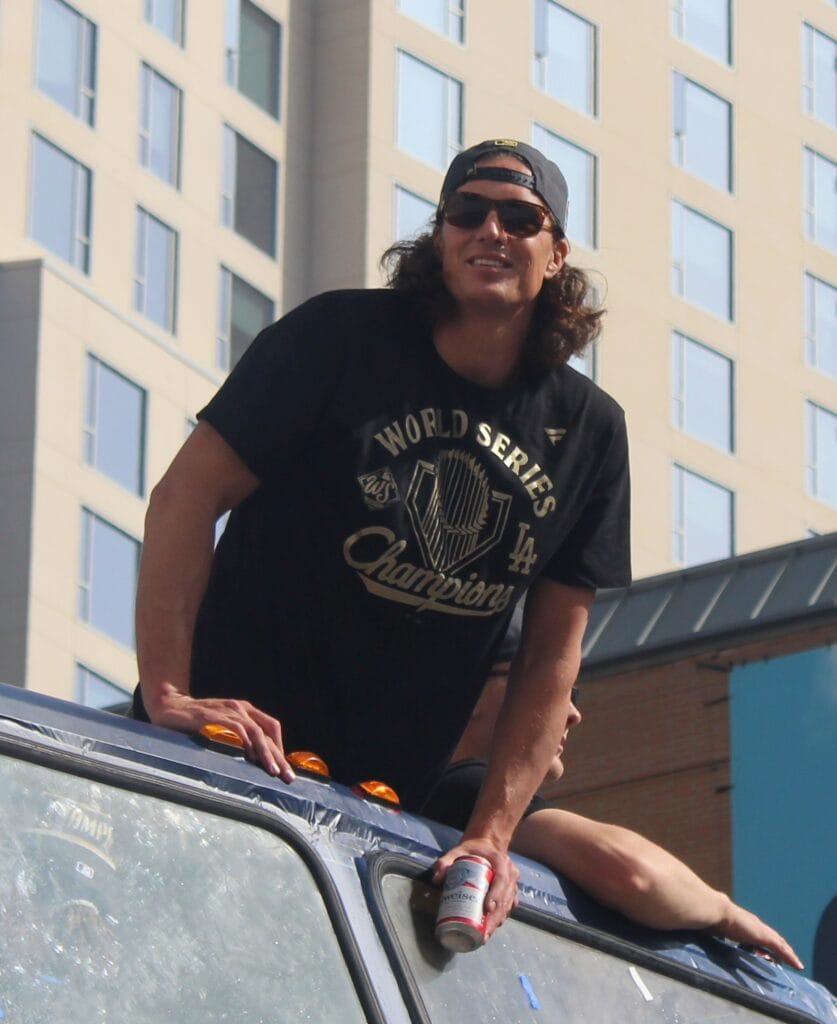 Tyler Glasnow with long hair and a World Series champions shirt leaning on a parade vehicle.
